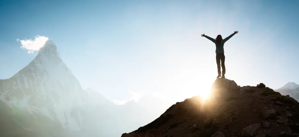 Person standing victorious on a mountain top at sunrise